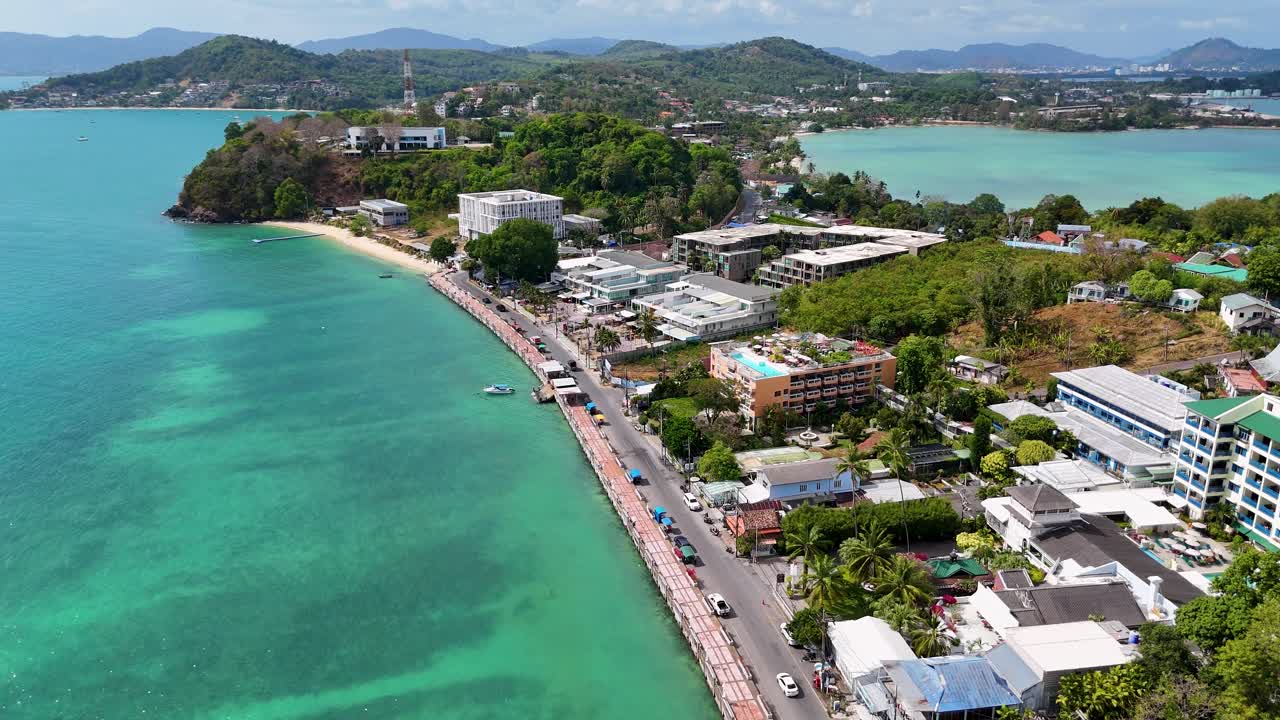 Drone footage captures the vibrant coastline and bustling streets of Patong Beach, Phuket, under bright daylight with clear skies