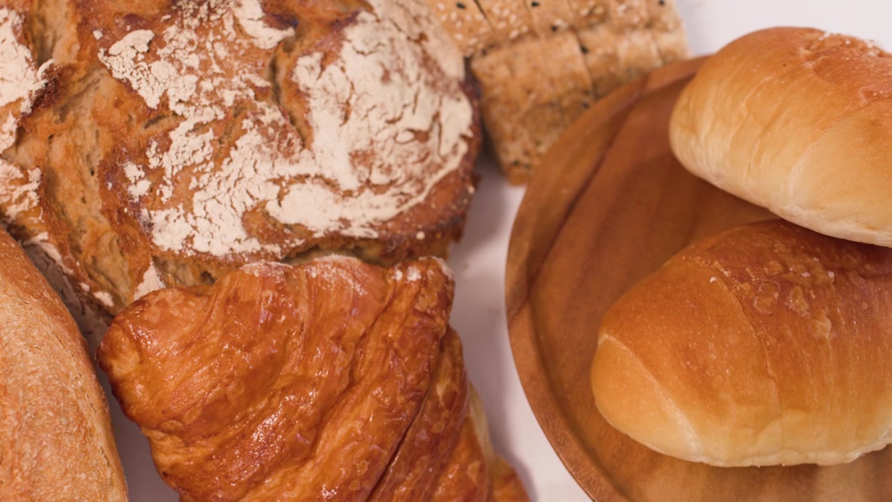 Close-up overhead view of rotating sourdough, croissants, and baguettes under warm studio lighting.