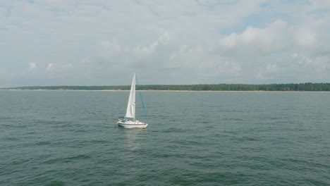 Aerial-establishing-view-of-a-white-sailboat-in-the-calm-Batltic-sea,-white-sailing-yacht-in-the-middle-of-the-boundless-sea,-sunny-summer-day,-wide-tracking-done-shot