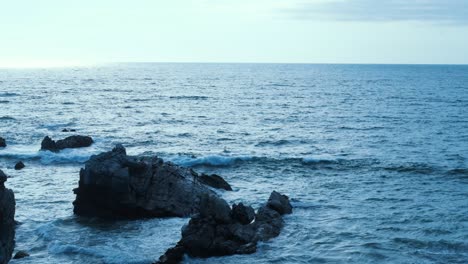 Stunning-slow-motion-capture-of-a-rugged-cliff-amidst-the-azure-embrace-of-the-ocean-along-Mexico's-coast,-portraying-a-tranquil-interplay-between-land-and-sea