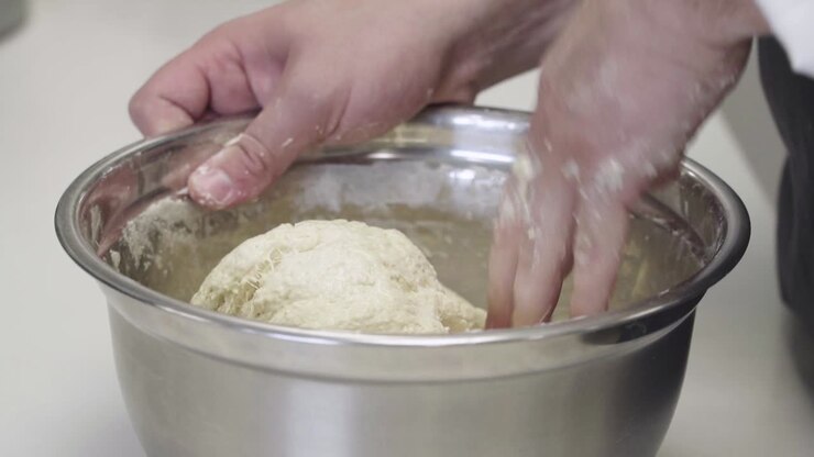 Close-up of hands mixing fresh dough in a metal bowl
