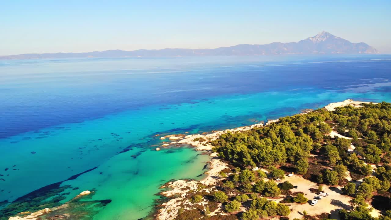 Aerial drone view of the Aegean sea rocky coast with blue transparent water, multiple greenery, mountain on the background. Greece