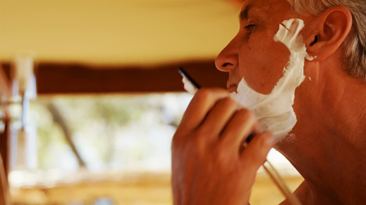 hombre afeitando su barba con una navaja de afeitar en la cabaña 4k