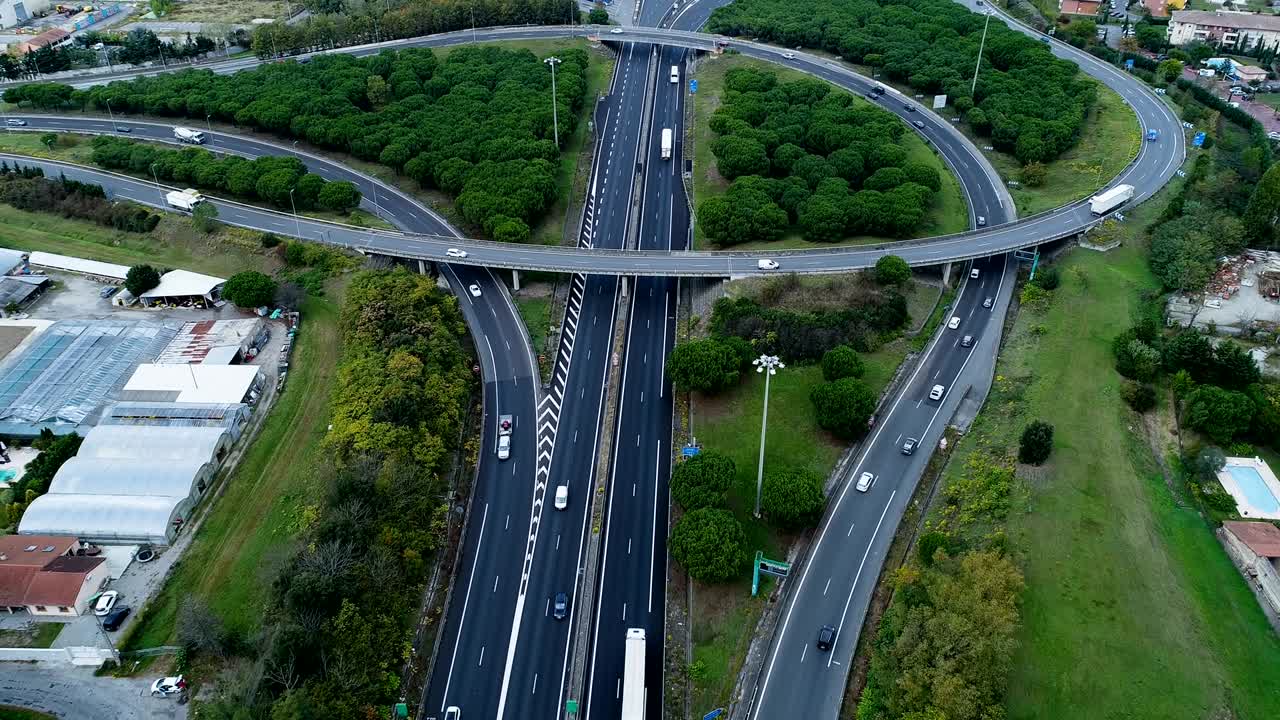 프랑스의 고속도로 교차로 위에서 공중에서 볼 수 있는 멋진 파노라마, 도로 주변의 집과 풀, 도로에서 운전하는 자동차와 트럭.