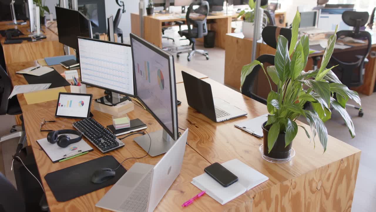 Oficina moderna vacía con gráficos en las pantallas de las computadoras y plantas en macetas sobre las mesas.