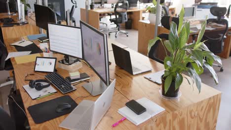 Empty-modern-office-with-graphs-on-computer-screens-and-plants-in-pots-on-tables