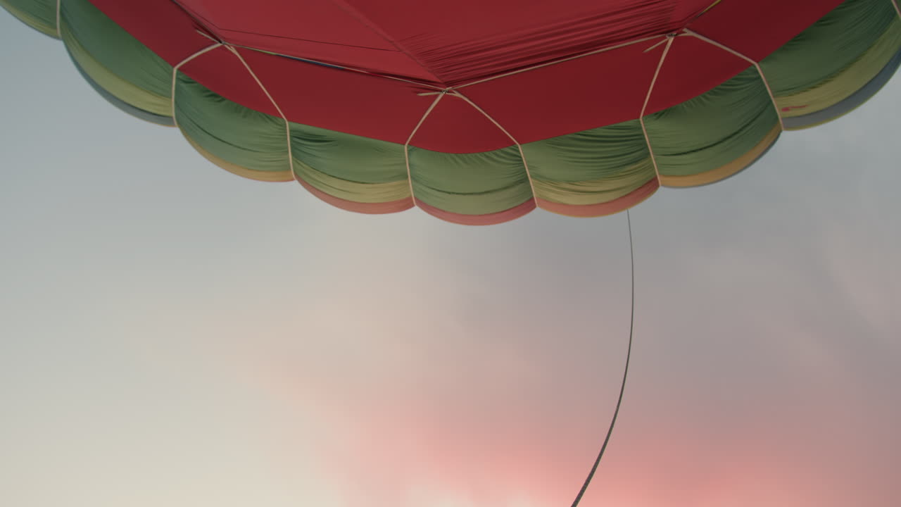 close up of rope extending from vibrant hot air balloon canopy against soft pastel sky during sunset showing colorful segments of balloon with gentle curve of rope floating through warm air