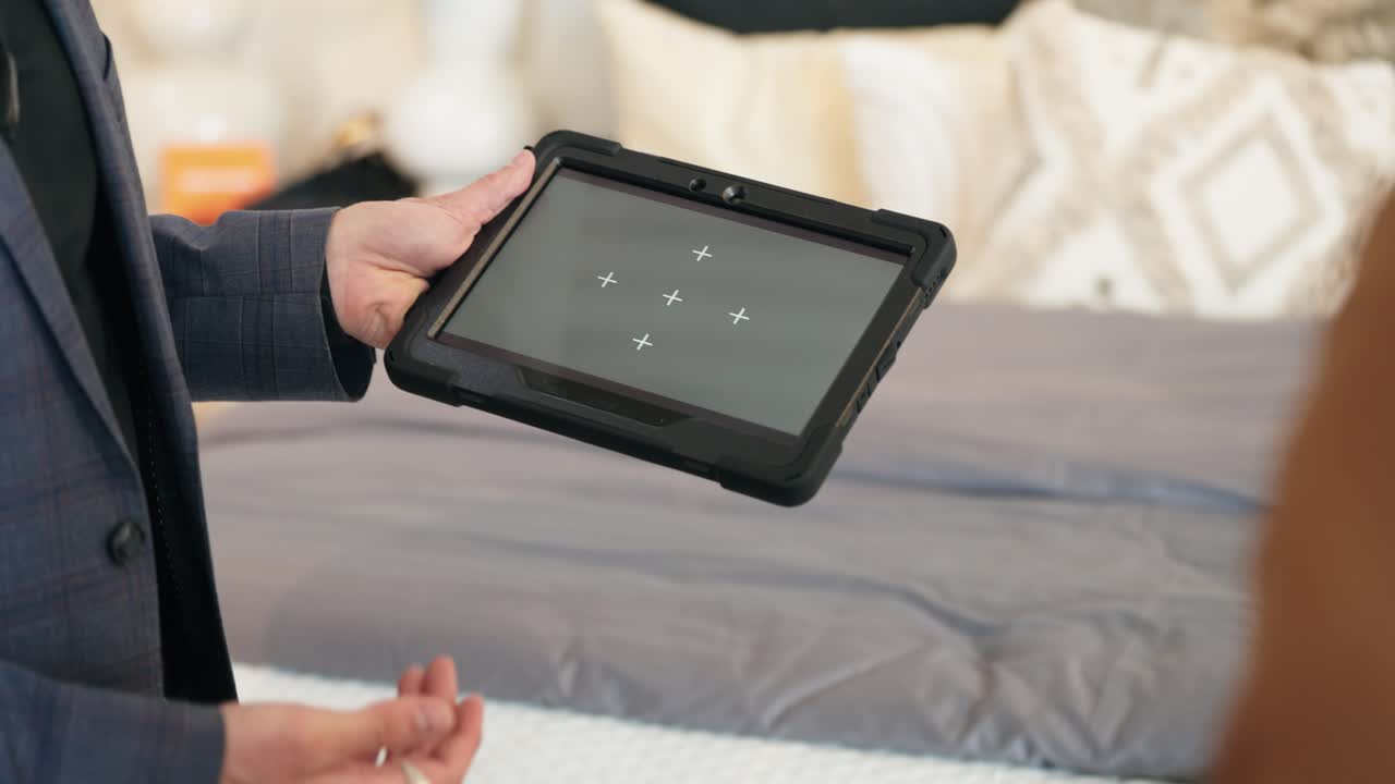 Camera tracks tablet as suited man lifts it from bed, showing tracking markers