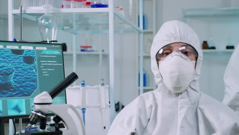 microbiologist sitting in laboratory wearing ppe suit looking at camera