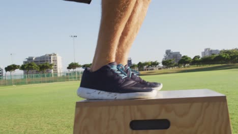 low section of fit caucasian man exercising outdoors jumping on box