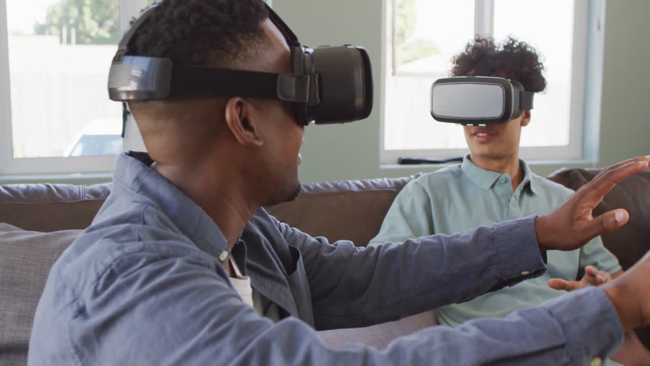 Happy diverse male friends using vr headset and talking in living room