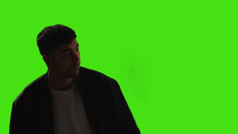 aburrido o harto joven de pie y esperando contra el fondo de la pantalla verde con iluminación de bajo nivel