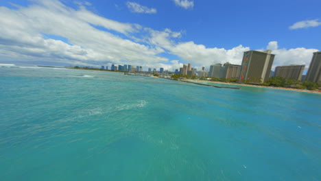 flying over waves on waikiki, fpv drone flying over blue pacific water towards waikiki and honolulu on bright summer day