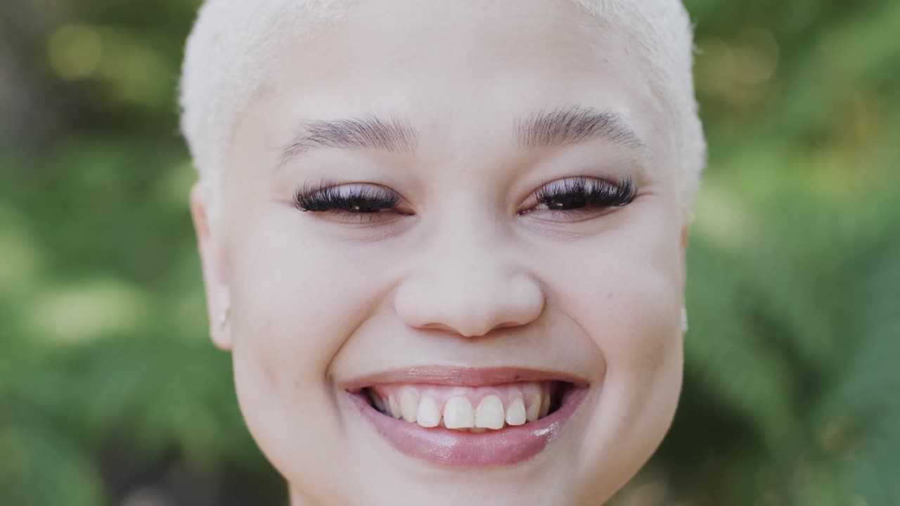 Portrait of happy biracial woman in garden with big green leaves in slow motion