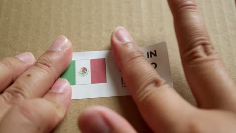 Hände-Bringen-Das-Etikett-„Made-In-Mexico“-Mit-Der-Flagge-„Made-In-Mexico“-Auf-Einem-Versandkarton-Mit-Einem-Barcode-In-Premiumqualität-An