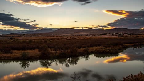 Zeitraffer-Einer-Wolkenlandschaft,-Die-Bei-Sonnenuntergang-Von-Einem-Glasigen-Fluss-Reflektiert-Wird,-Mit-Bergen-In-Der-Ferne