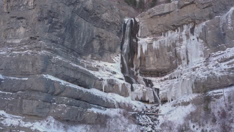 a half frozen half flowing waterfall flowing down rugged terrain in the rocky mountains