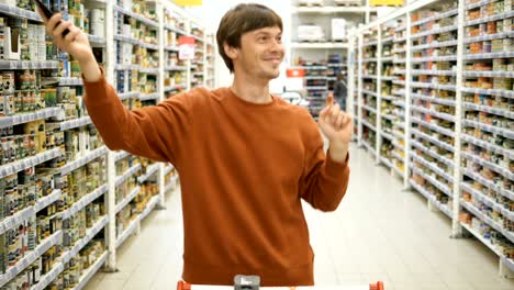 happy guy in brown sweatshirt dances holding smartphone in shop