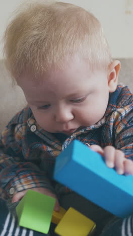 cute blue eyed boy plays with bright cubes sitting on large soft bed in light children room close view