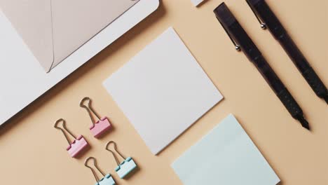 Overhead-view-of-notebook,-pens-and-stationery-arranged-on-beige-background,-in-slow-motion