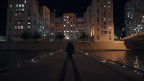 the girl is on the small bridge and approaching l'arbre blanc at night, montpellier - france