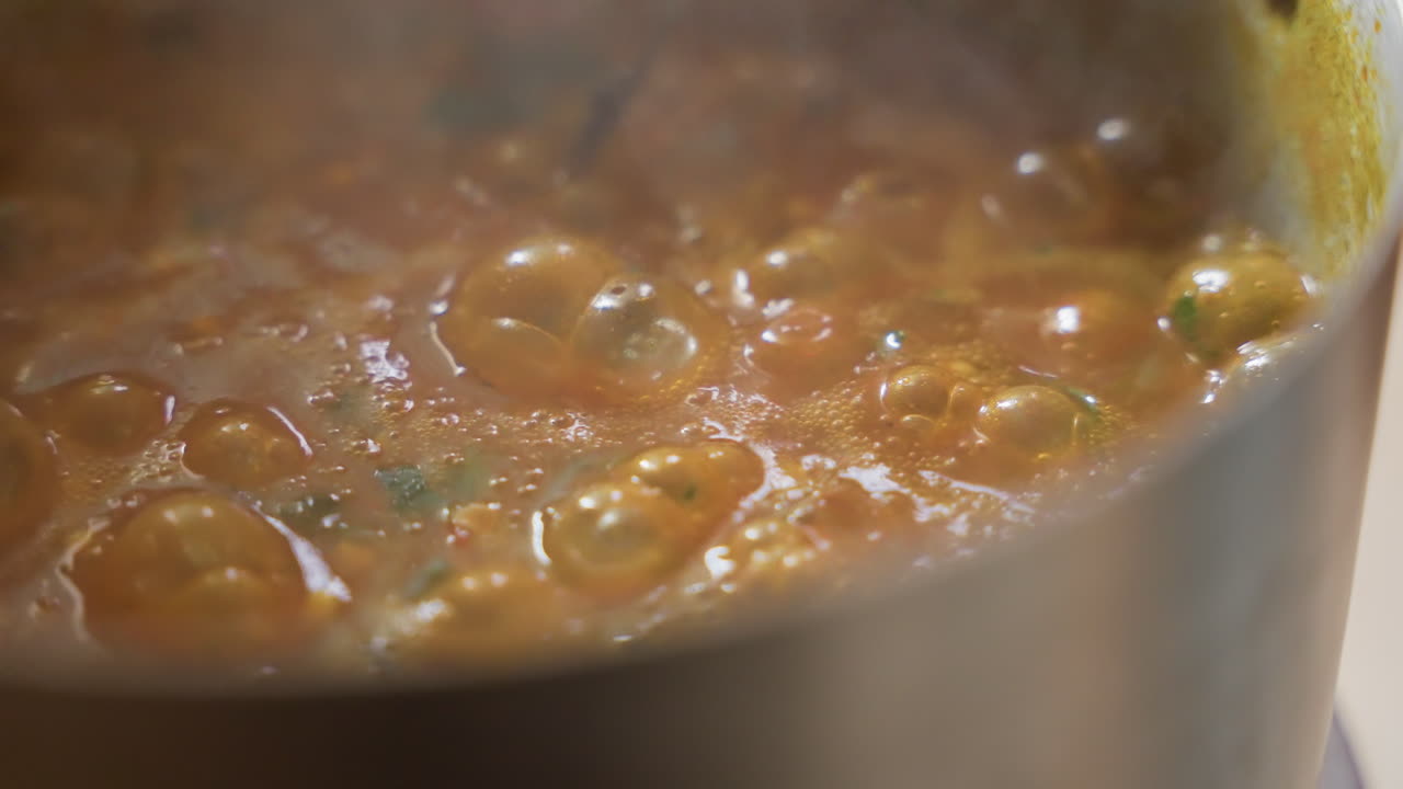 Curry dorato e cremoso che bolle in pentola, chef che finisce la salsa con una lenta mescolata, vapore che sale e bolle arrotondate che si formano, consistenza vellutata con note di curcuma e cocco, riduzione delicata e brodo ricco
