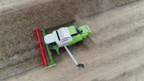 rotating aerial drone view of the grain discharge arm extending on a claas tucano combine harvester and then discharging rapeseed from the onboard hopper into a waiting tractor trailer unit.