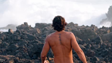 a man walks through jagged volcanic rocks in timanfaya national park, lanzarote, while powerful ocean waves crash in the background.