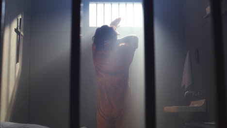 bored inmate wandering around sunlit prison cell, then taking seat on bed