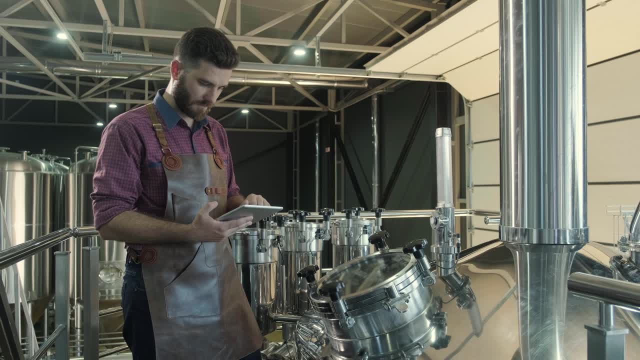 un joven cervecero con un delantal de cuero supervisa el proceso de fermentación de la cerveza en una fábrica de cerveza moderna