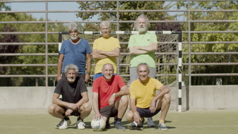 portrait of a senior football team posing on the field, giving five to each other and looking at the camera