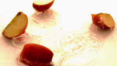 cuartos de manzana cayendo y rebotando en una superficie blanca y húmeda