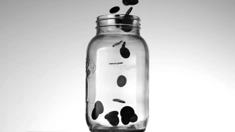 many coins pouring into glass jar on white background