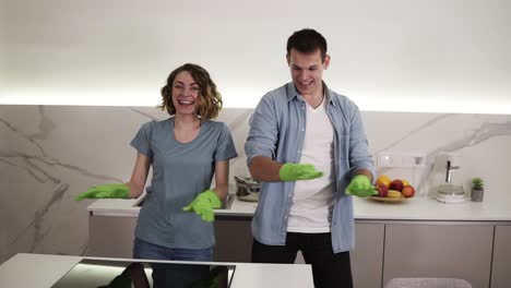 pareja feliz bailando sincrónicamente en la cocina ambos con guantes de goma verdes divirtiéndose en el día de limpieza en el apartamento estudio. movimientos divertidos. juventud moderna, la gente y el concepto de limpieza