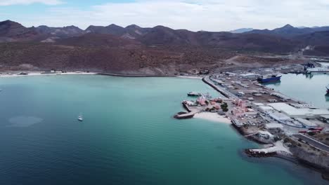 Vista-Panorámica-Aérea-De-Playa-Pichilingue-Cerca-Del-Ferry-Y-Puerto-De-Cruceros-De-La-Paz,-Baja-California-Sur,-México-Con-Playa-De-Arena,-Costa-Idílica,-Edificios-Históricos-Y-Montañas-Majestuosas