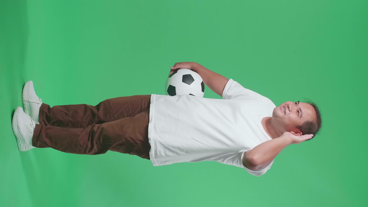 초록색 스크린 배경에서 축구를 응원하는 동안 듣기 위해 공을 는 아시아 남자의 몸이 가득 차 있습니다.