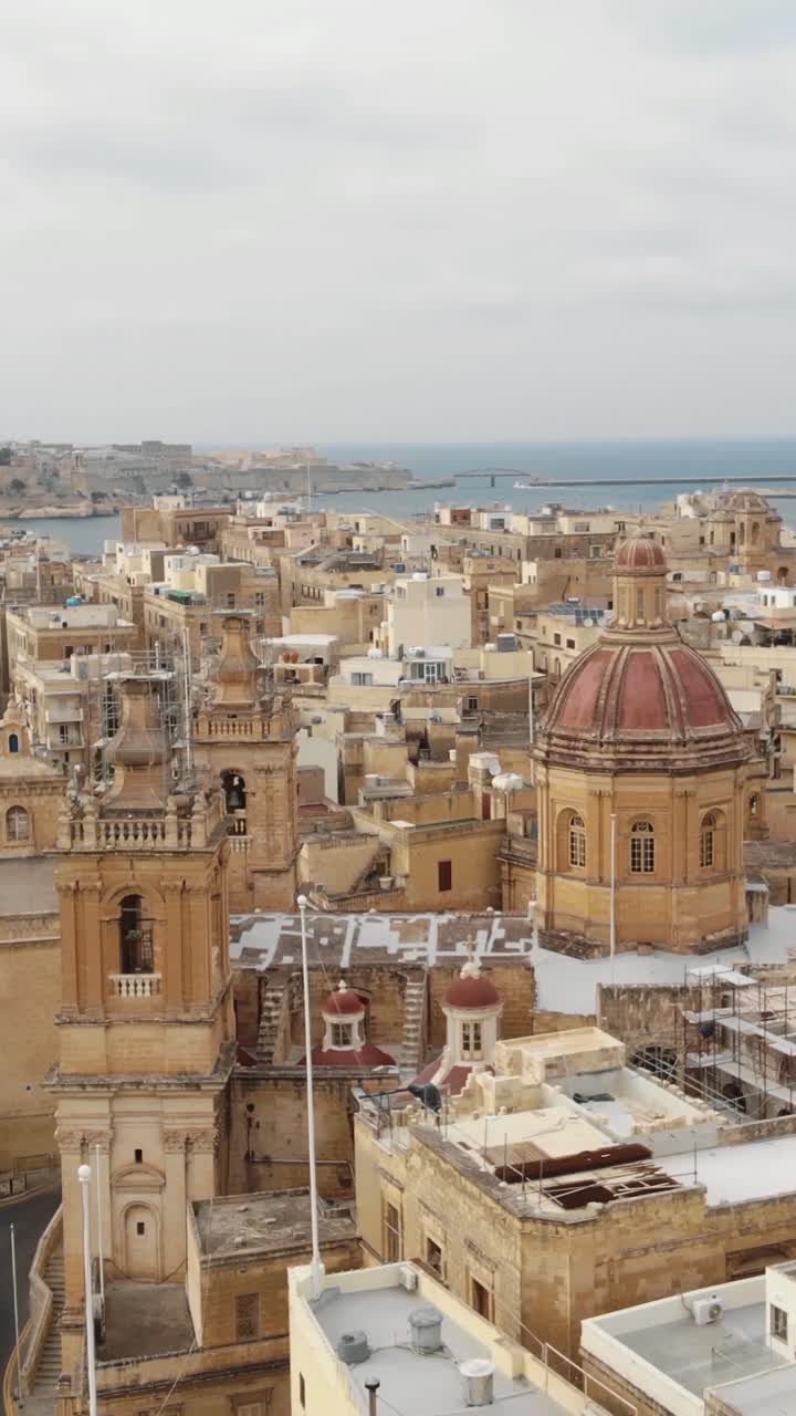 Picturesque cityscape of Vittoriosa, Malta, featuring the prominent dome of St Lawrence Collegiate Church amidst traditional Maltese architecture. Aerial, vertical shot