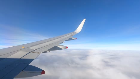 Vista-De-La-Ventana-Del-Avión,-Ala-Volando-Sobre-El-Mar-De-Nubes-Bajo-Un-Cielo-Azul-Claro