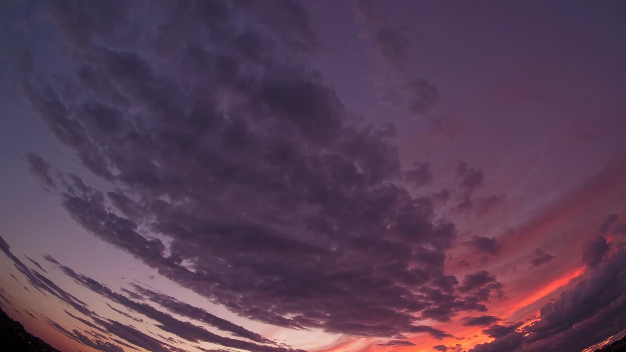 Fisheye lens captures a dramatic sunset sky with swirling clouds, creating a surreal, immersive