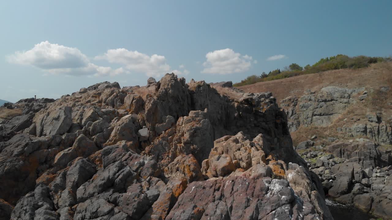 화창한 여름날 해변의 큰 바위 위로 공중 추적 촬영