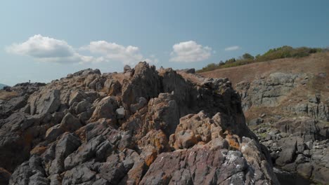 Tiro-De-Seguimiento-Aéreo-Sobre-Grandes-Rocas-En-La-Orilla-Del-Mar-En-Un-Día-Soleado-De-Verano