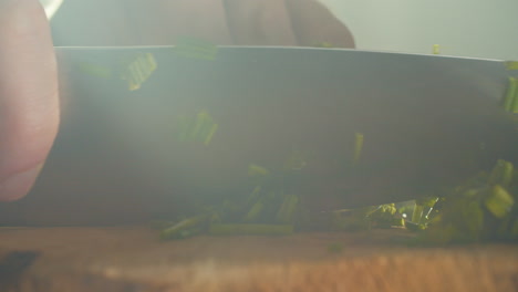 close shot of a male hand starting to cut chives on a wooden cutting board in a smoky kitchen atmosphere