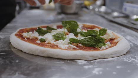 primo piano mettendo il basilico fresco sopra l'impasto della pizza napoletana preparato sul tavolo da cucina della pizzeria