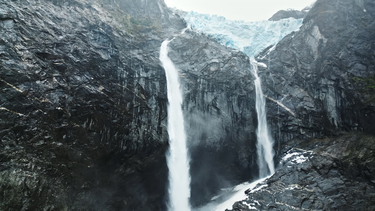 Aerial drone view of twin waterfalls flowing down rocky cliffs from a massive glacier in Patagonia
