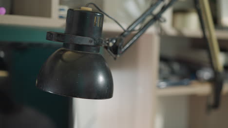 a close-up view of a technician's hand in a black glove adjusting a lamp, with a blurred background showing a shelf