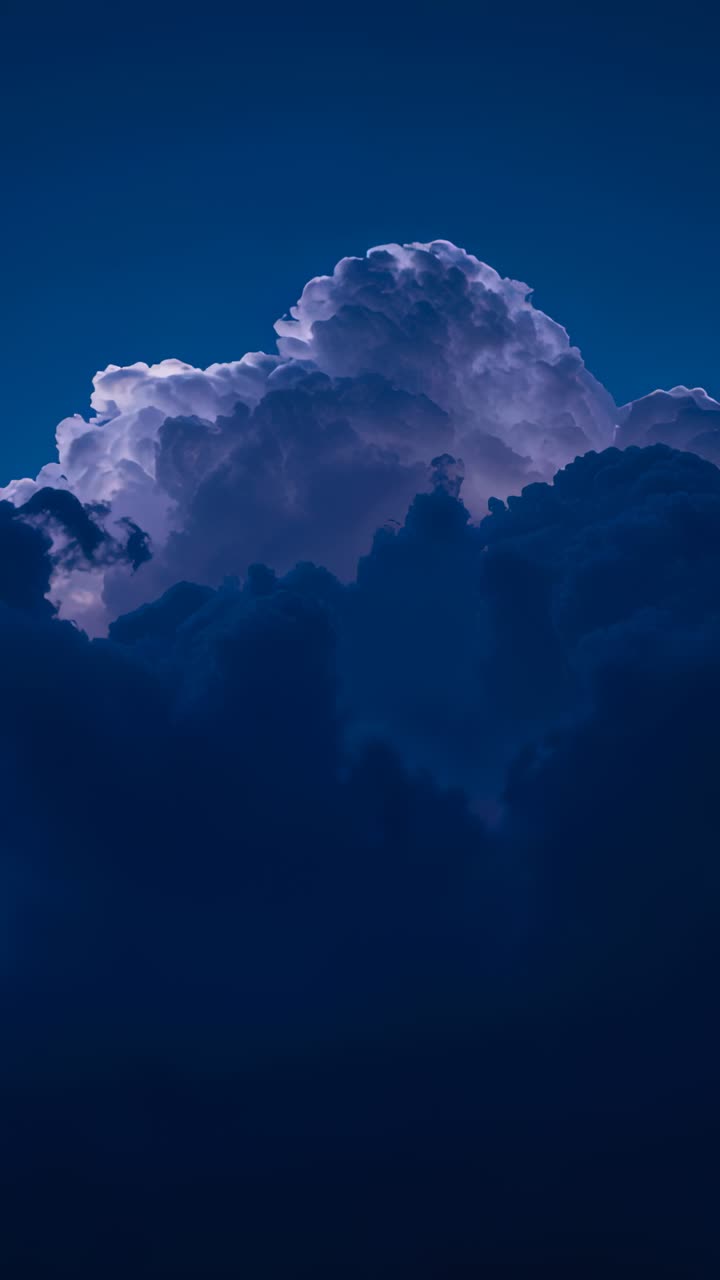 Vertical video: Growing cumulonimbus cloud rising through twilight sky, rim lighting revealing dome