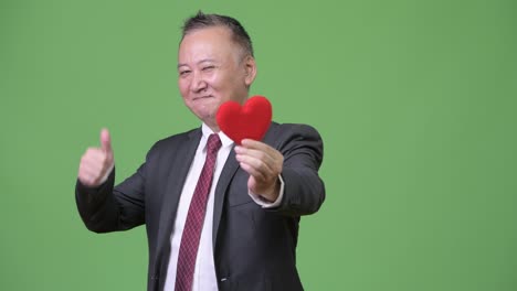 발렌타인 데이를 위해 준비된 은 심장을 들고 있는 성숙한 일본인 사업가