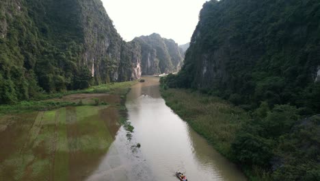 tourists on tour boats paddling on ngo dong river at limestone ravine in ninh binh national park, flooded rice fields on river banks - aerial dolly