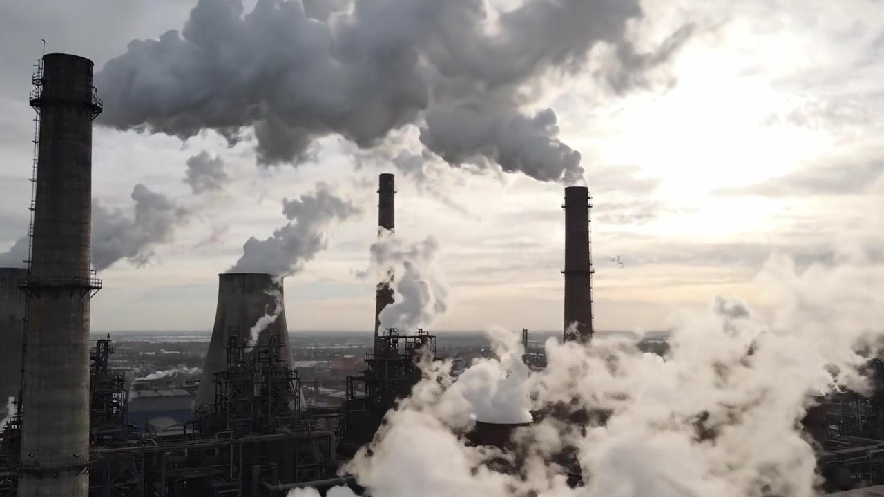 Complesso Industriale: Vista Aerea di Ciminiere che Scaricano Vapori ed Emissioni Sotto un Cielo Nuvoloso, Evidenziando le Preoccupazioni Ambientali nelle Regioni Manifatturiere