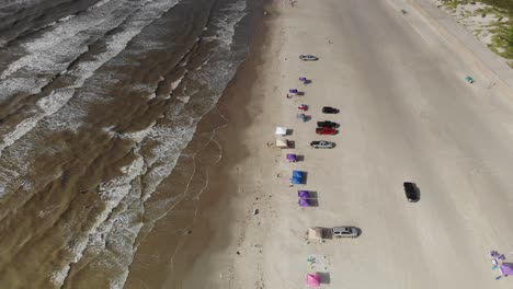 Angled-view-of-the-ocean-and-beach-with-no-skyline,-Moving-towards-the-water-over-several-tents-and-cars